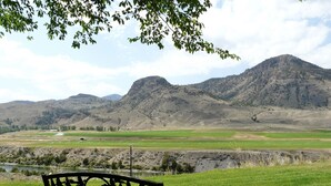 Un banco en un área verde con vistas a una cadena montañosa y un río al fondo.