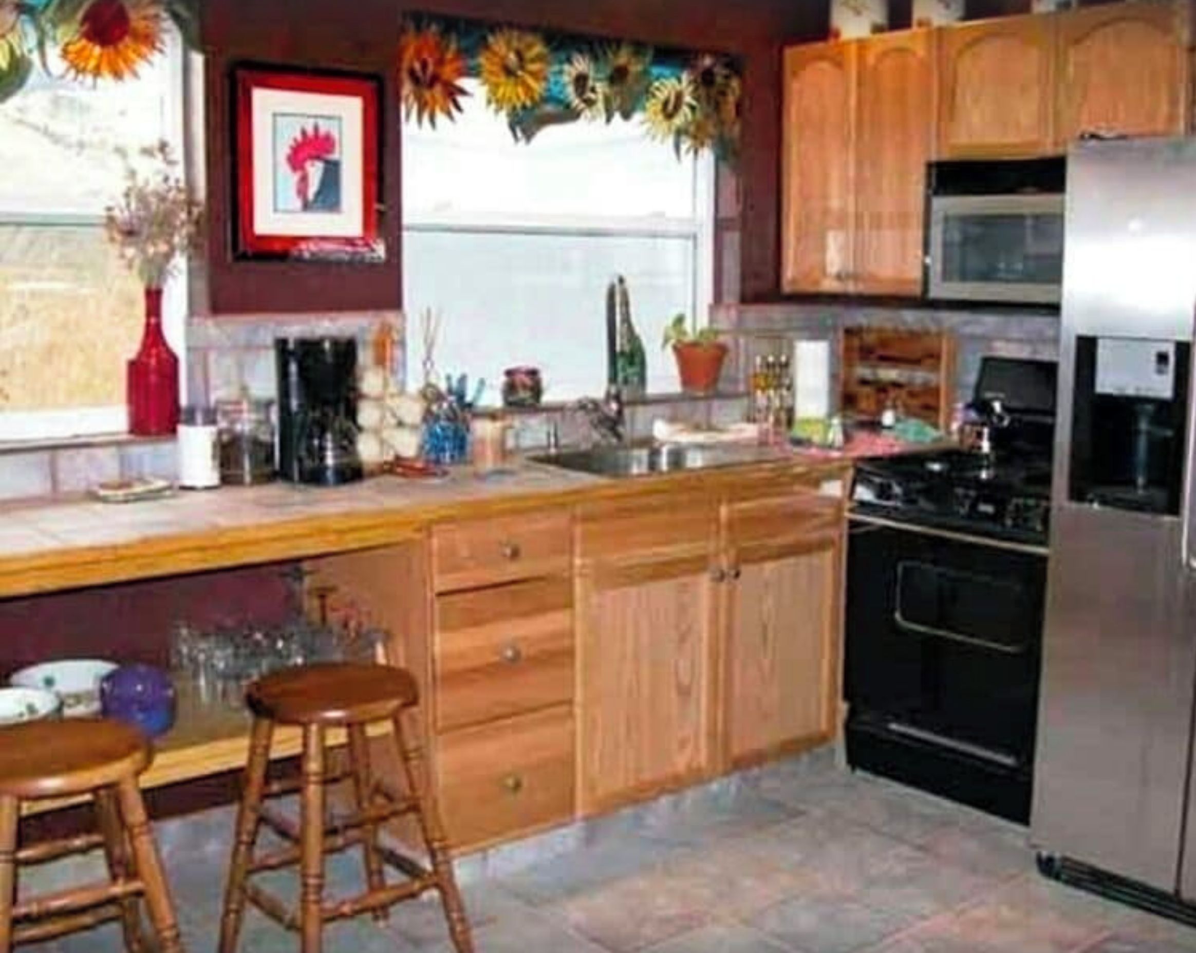 Une cuisine avec des meubles en bois, un réfrigérateur en acier inoxydable, un four à micro-ondes et une cuisinière. On y trouve deux tabourets en bois et un vase avec des fleurs sur le comptoir.