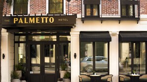 The exterior of The Palmetto Hotel with a black awning, large glass doors, and outdoor seating area with chairs and tables. - The Palmetto Hotel (Charleston)