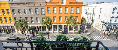A multi-story building with a yellow, brown, and orange facade, featuring a central entrance with a large window and a small balcony with plants.