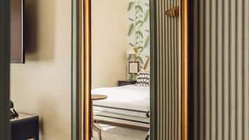 A room with a large mirror, a bed, a bedside table, a lamp, and a television.
