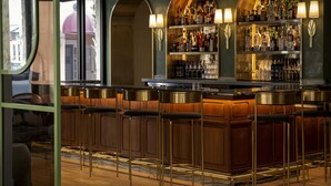 A bar area with wooden bar stools, a counter, and shelves stocked with bottles and glasses. - The Palmetto Hotel (Charleston)