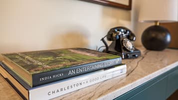 A stack of books on a marble countertop with a vintage telephone and a lamp in the background.