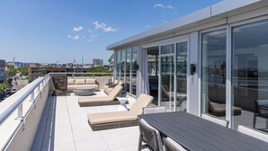 A rooftop terrace with sun loungers, a table, and a glass-enclosed area. - The Palmetto Hotel (Charleston)