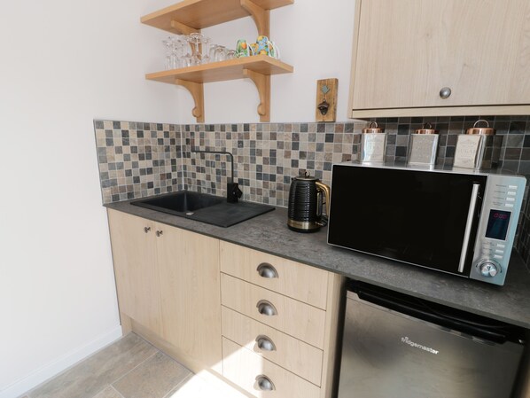 A kitchen with a black sink, a coffee maker, a microwave, and a dishwasher. - Drws y Gorlan (Llanerchymedd)