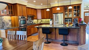 A modern kitchen with wooden cabinets, stainless steel appliances, a marble backsplash, and a bar area with stools.