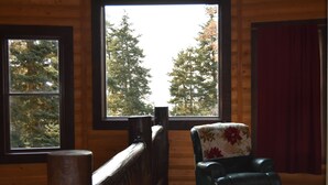 A room with a large window, a wooden chair, and a red curtain.