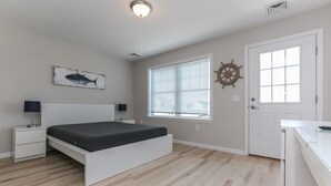 Een slaapkamer met een bed, nachtkastjes, een raam met zonwering, een deur en een wanddecoratie.