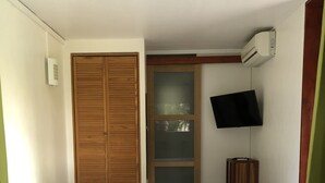 A bedroom with a bed, wooden wardrobe, a television, and an air conditioning unit.