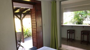 A room with a bed, a sliding glass door to a balcony, and two wooden stools.