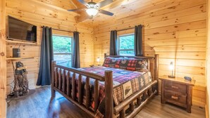 A wooden cabin bedroom with a bed, a ceiling fan, a TV, and a nightstand. - Incredible Views, Hot Tub, Pool Table, Waterfalls, Hiking (Bryson City)