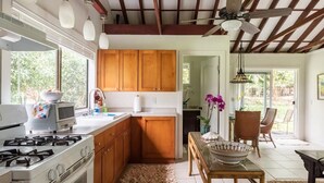 A kitchen with wooden cabinets, a gas stove, and a dining area with a table and chairs. - JJs Hāna Hale - Farm House (Hana)