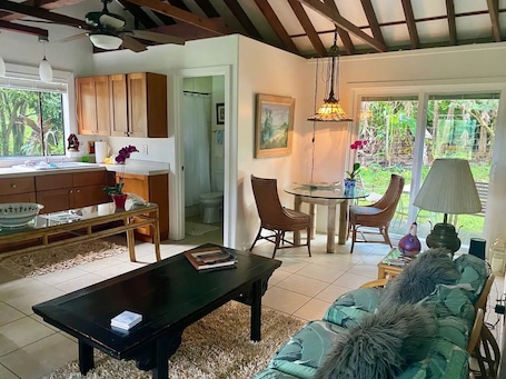 A cozy living room with a sofa, a coffee table, and a dining area with chairs and a table. There is a kitchen visible in the background.