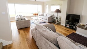 A spacious living room with a large TV, comfortable seating, and a view to the outside. - Curragh Hill (Mulranny)