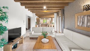 Een moderne woonkamer met een houten plafond, een flatscreen televisie op een houten dressoir, een houten salontafel met een decoratieve schaal, en een witte bank.