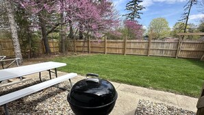 En trädgård med en grill, ett picknickbord och ett staket av trä.