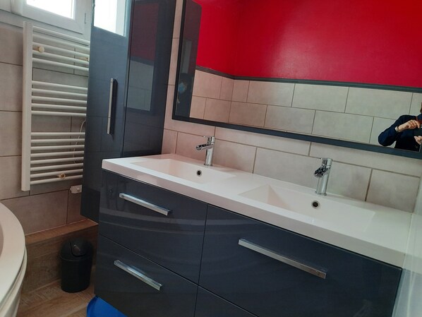 Een moderne badkamer met een wastafelmeubel met twee wasbakken, een grote spiegel en een rode accentmuur.