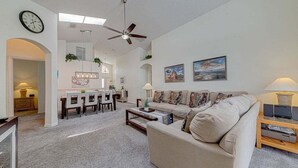 A living room with a sofa, coffee table, and a dining area with chairs and a table. - 10 - Beautiful home with Sparkling Pool & Games Room Near Disney Parks (Clermont)