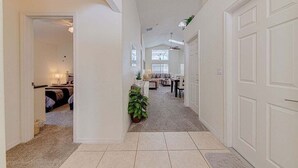 A hallway with a carpeted floor, a door on the right, and a room with a bed and a lamp in the background. - 10 - Beautiful home with Sparkling Pool & Games Room Near Disney Parks (Clermont)