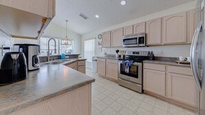 A modern kitchen with light wood cabinets, stainless steel appliances, and a large island. - 10 - Beautiful home with Sparkling Pool & Games Room Near Disney Parks (Clermont)