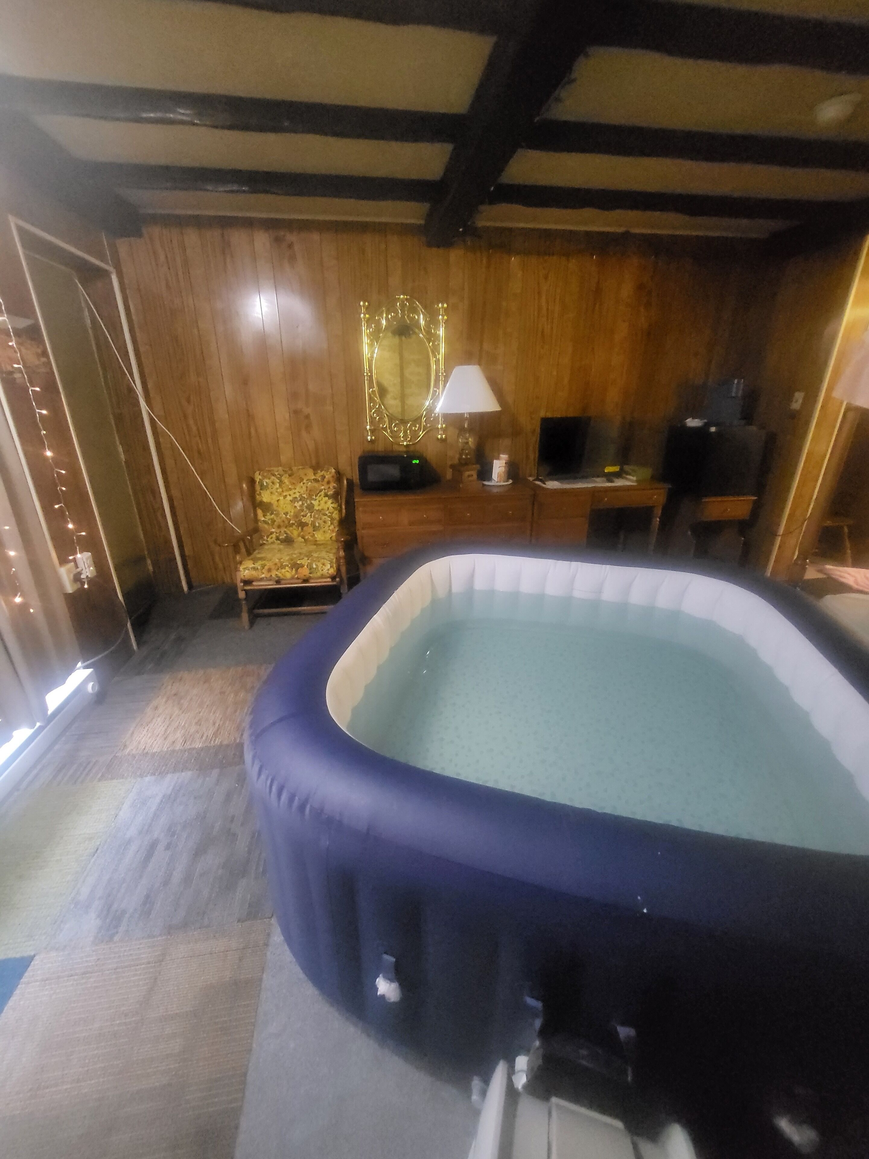 A room with a hot tub, wooden walls, a chair, a desk, and a television.