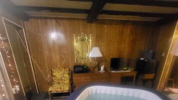 Een kamer met een bubbelbad, houten wanden, een stoel, een bureau en een televisie.