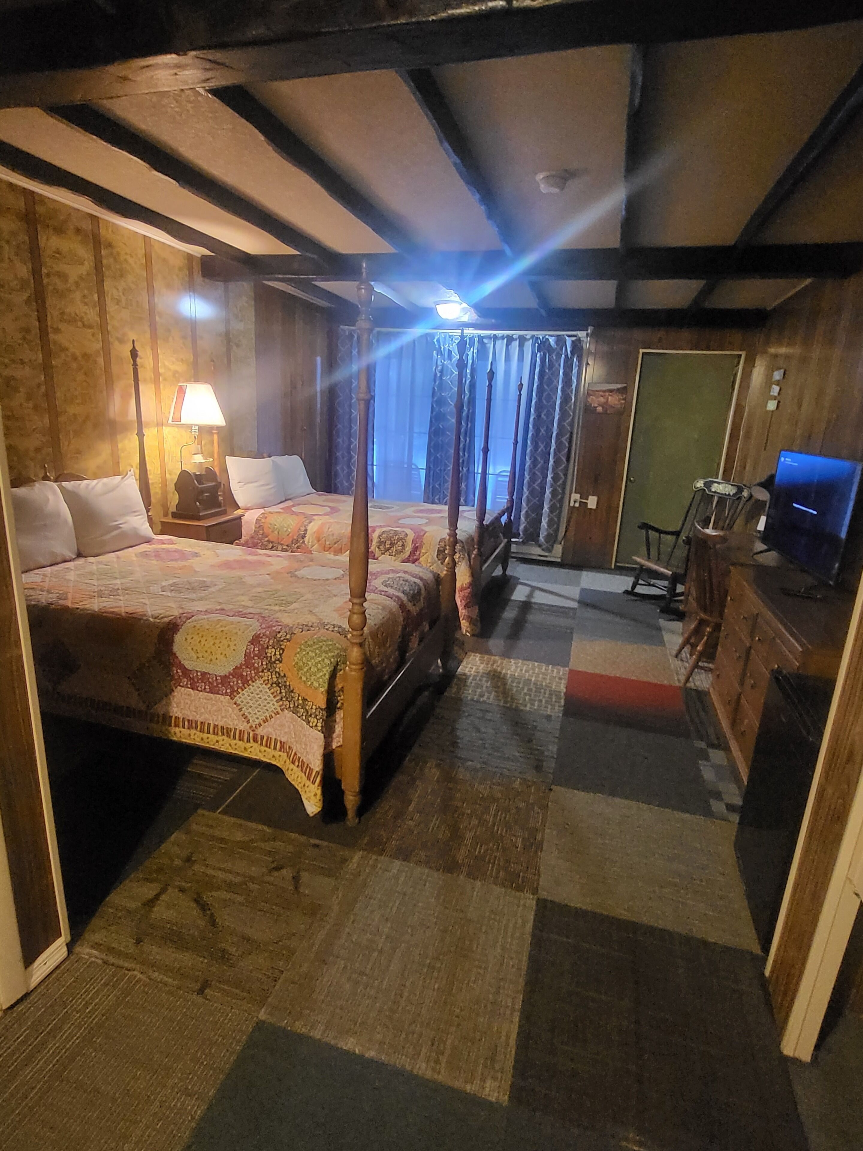 A traditional four-poster bed with a patterned bedspread, a bedside lamp, and a wooden nightstand.