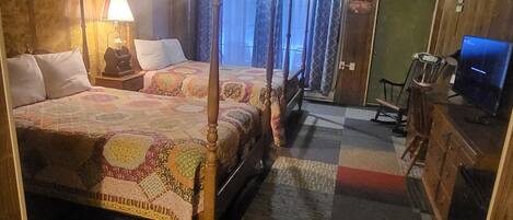 A traditional four-poster bed with a patterned bedspread, a bedside lamp, and a wooden nightstand.