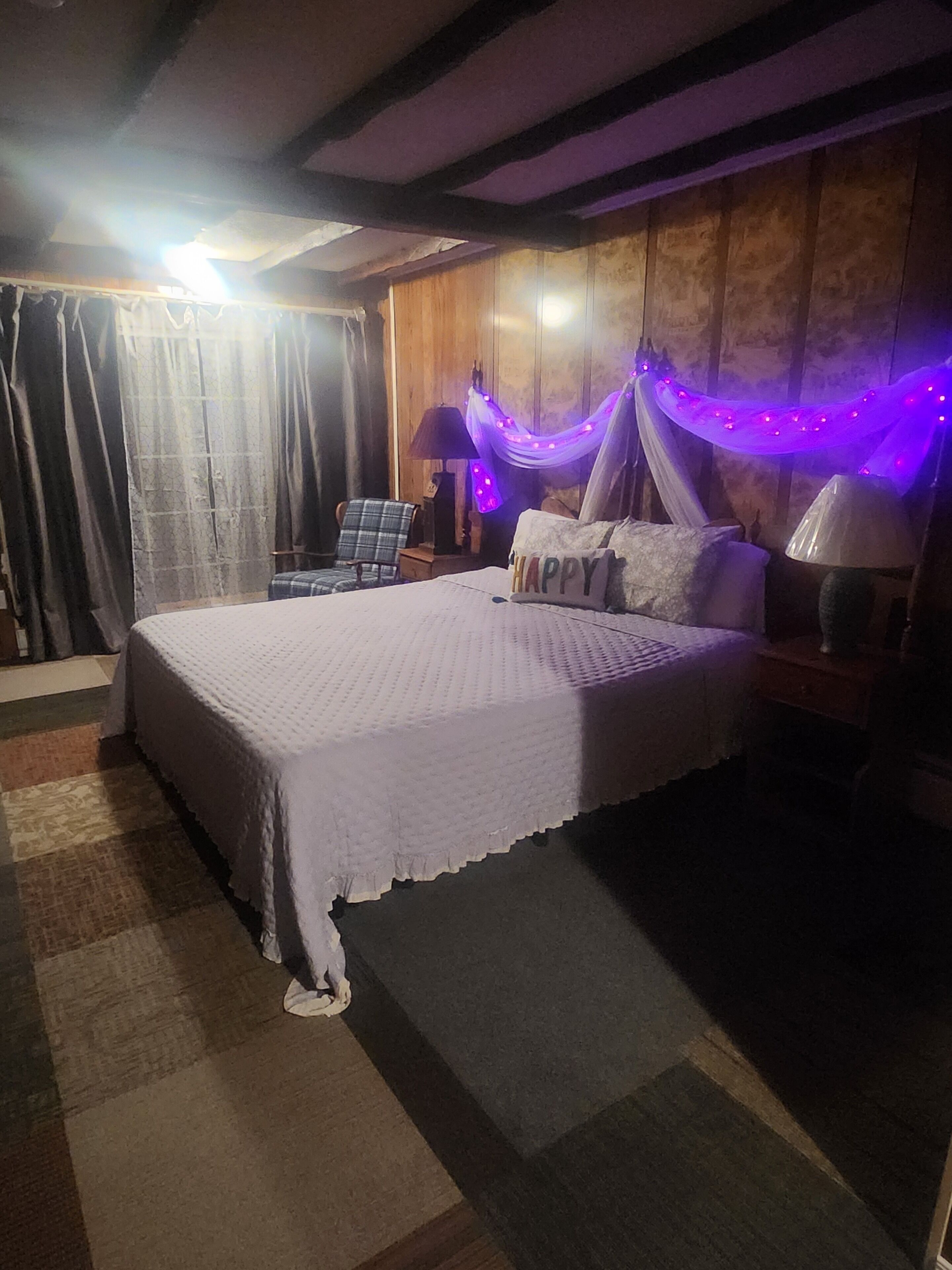 Une chambre bien rangée, avec un grand lit, une chaise, une table de chevet et une lampe.