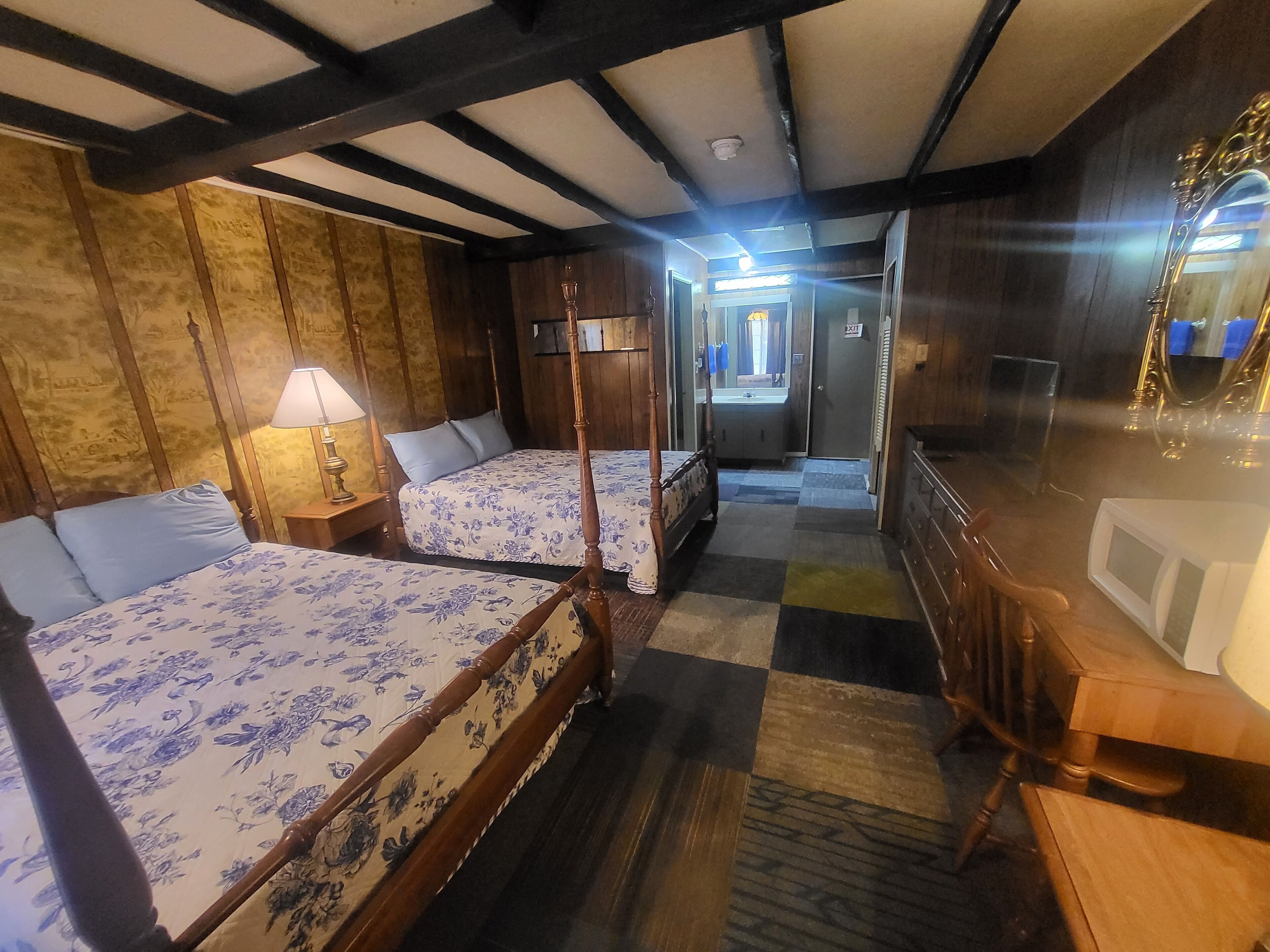 Une chambre avec deux lits, un bureau et un miroir. On aperçoit une salle de bain au fond.