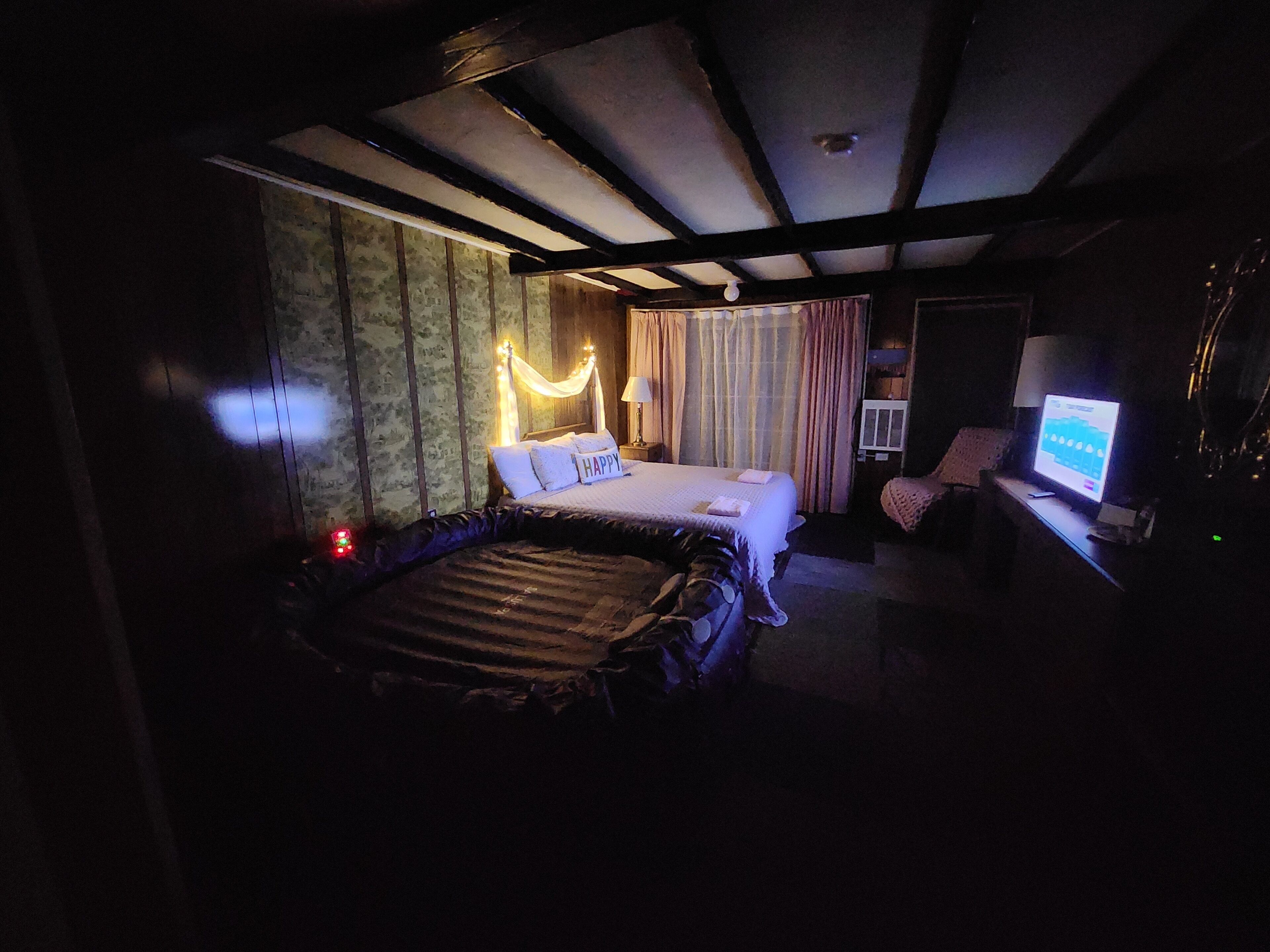 A dimly lit hotel room with a bed, a desk with a computer, and a TV.