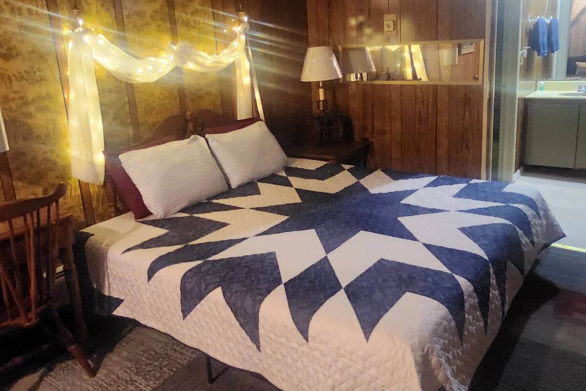 A bedroom with a large bed, wooden walls, a nightstand, a chair, and a small table.