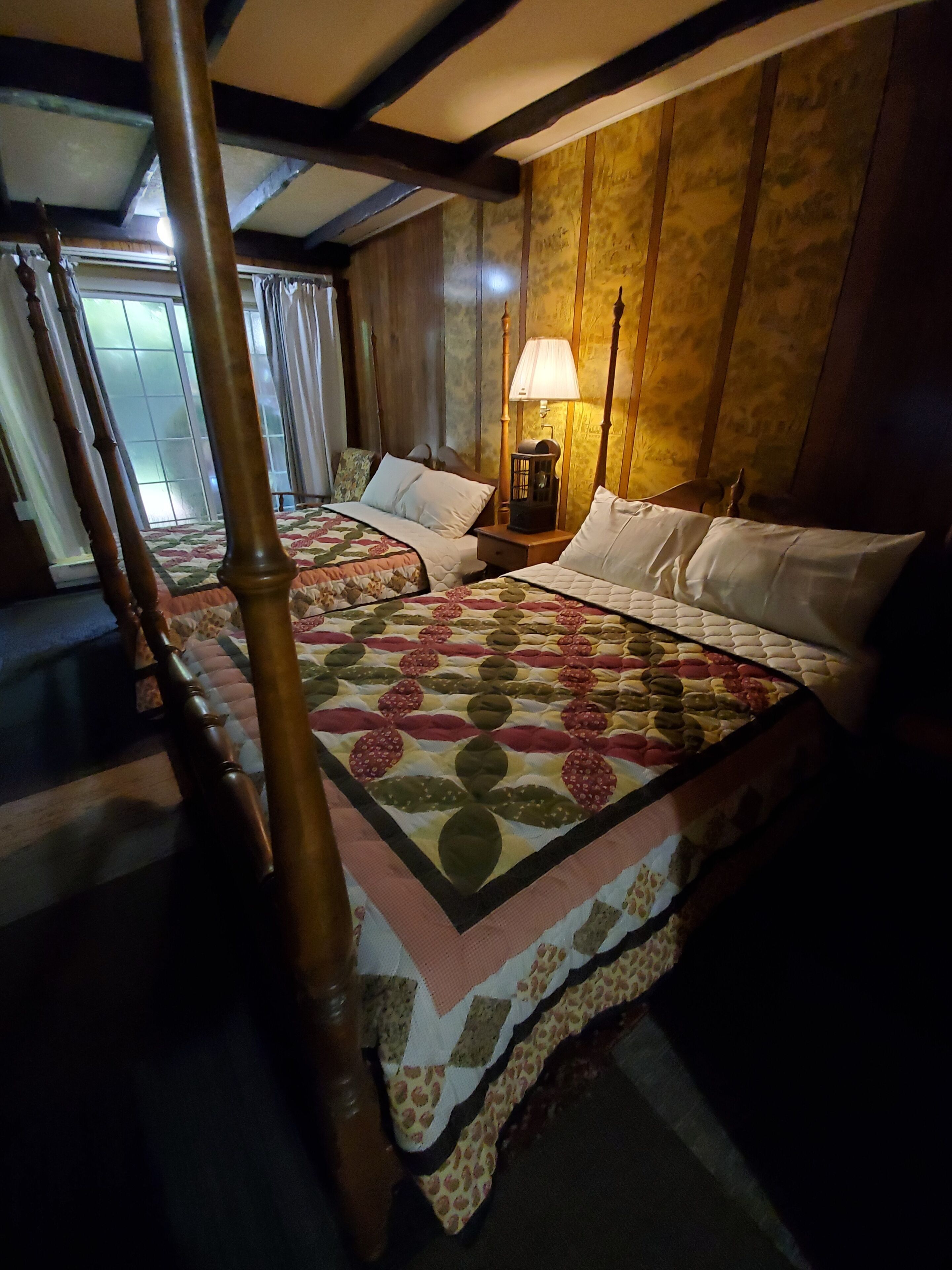 Une chambre avec un lit à baldaquin, une table de chevet avec une lampe et une fenêtre avec des rideaux.