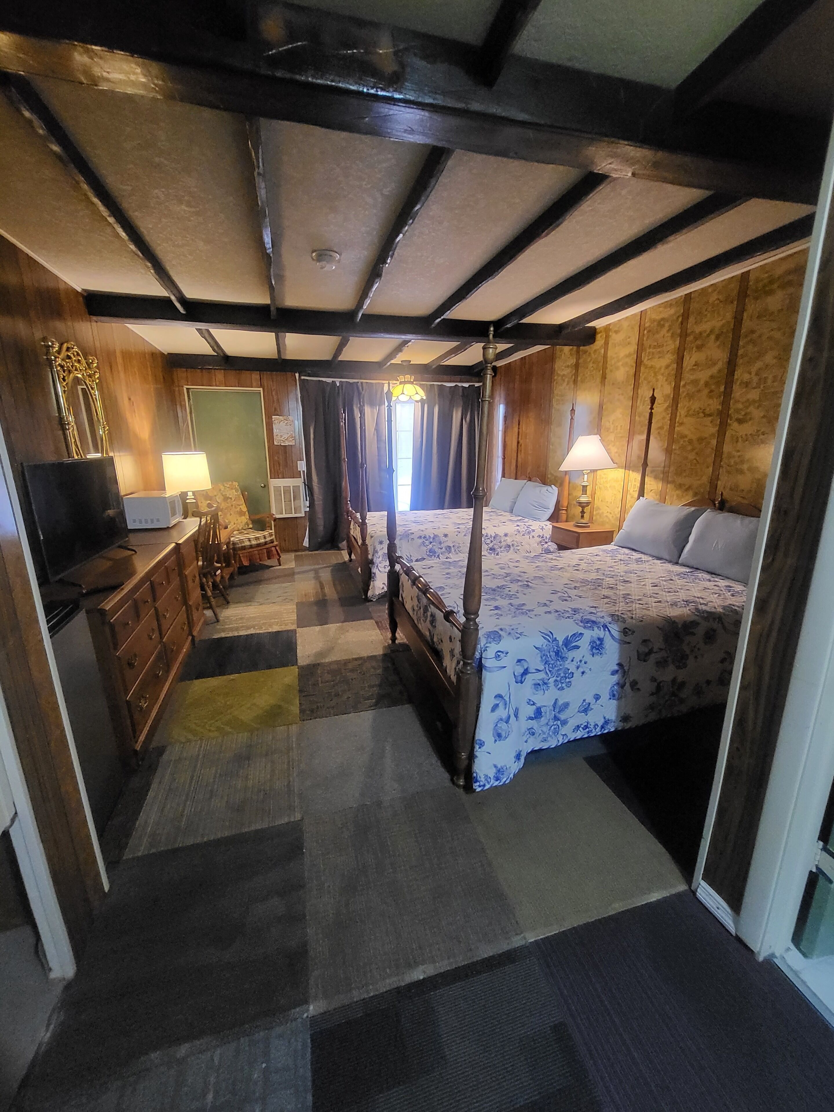 A traditional room with a four-poster bed, wooden furniture, and a checkered floor.