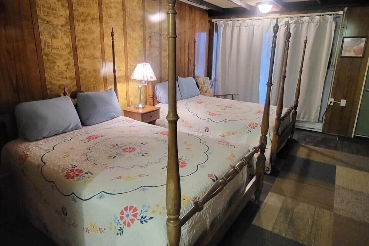 A four-poster bed with a floral bedspread, a nightstand with a lamp, and a wooden ceiling with exposed beams.