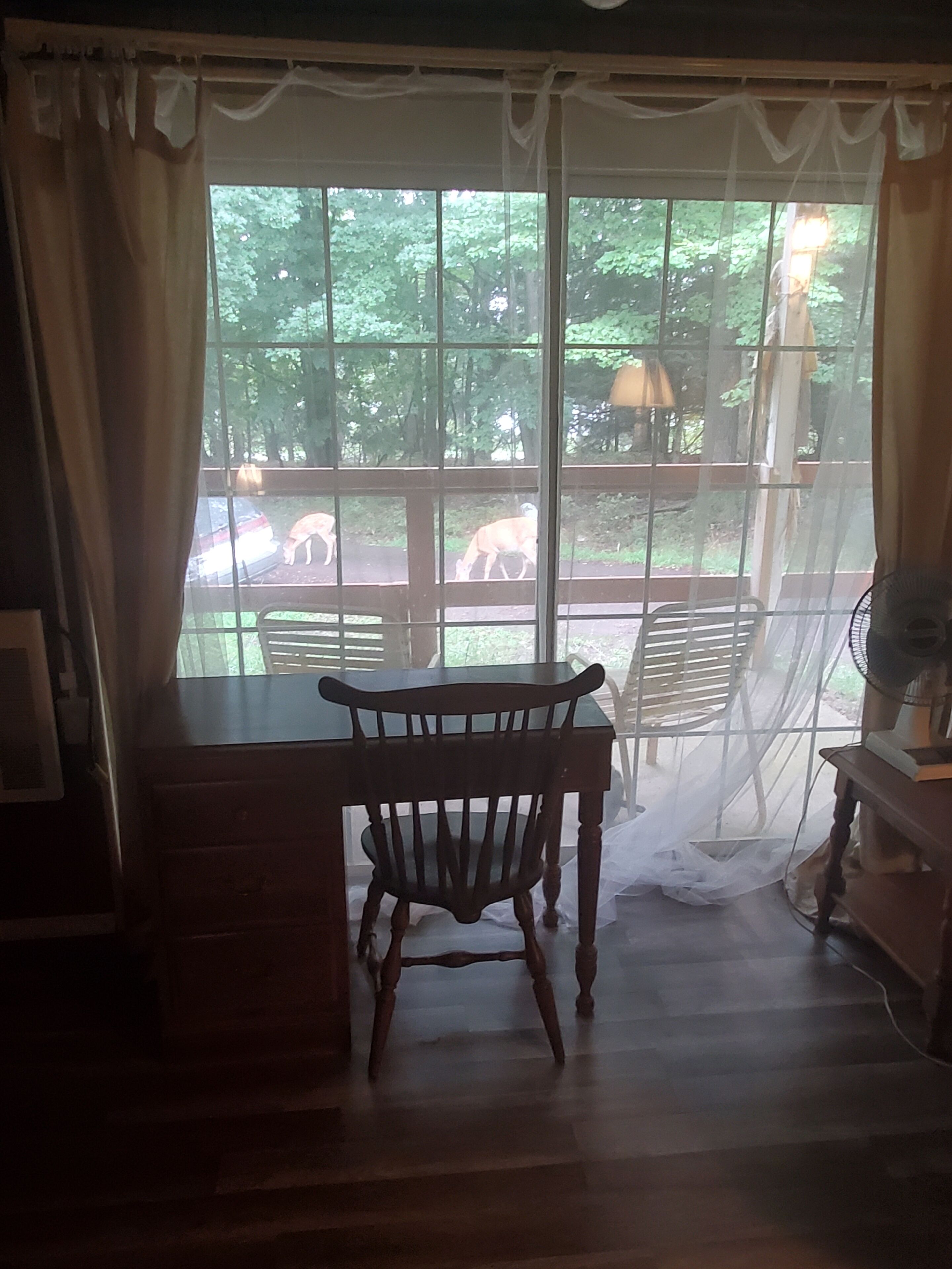 Una silla de madera en una habitación con un ventanal, cortinas y un ventilador.