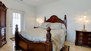 A bedroom with a wooden bed, bedside lamps, a dresser, and a door with a window. - Sunset bay view 1 (Pass Christian)