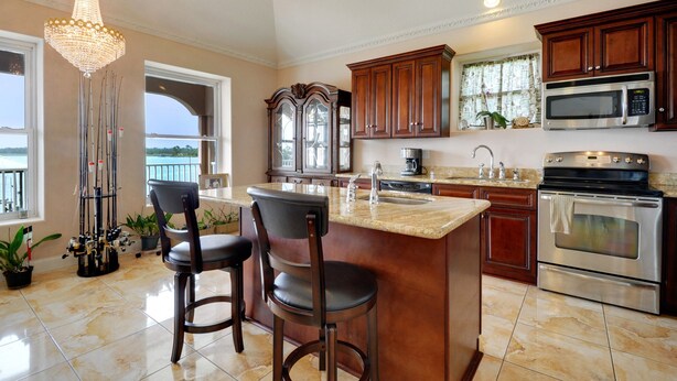 A kitchen with a large island, bar stools, a chandelier, and a view of the outdoors. - Sunset bay view 1 (Pass Christian)