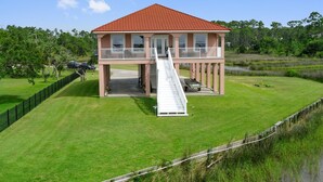 A two-story building with a red roof and a white staircase leading to a balcony. - Sunset bay view 1 (Pass Christian)