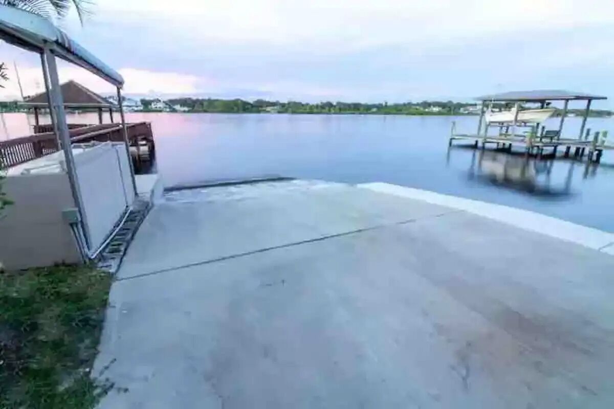 A waterfront property with a dock, a covered seating area, and a concrete pathway leading to the water.