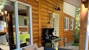 Een vakantiehuisje van hout met een terras, rieten meubilair en een barbecue.