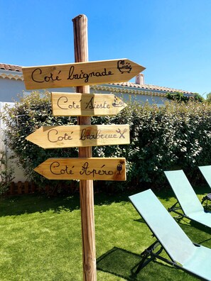 Un panneau indicateur en bois, orné de flèches indiquant différentes directions : Côte Brignade, Côte Sieste, Côte Barbecue et Côte Aventure.