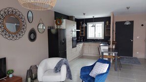 Una cucina moderna con un frigorifero nero, mobili in legno e un'area pranzo con una sedia blu e un divano bianco.
