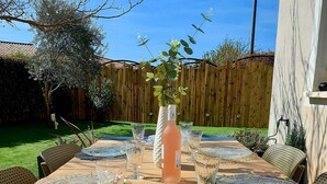 Un tavolo da pranzo all'aperto apparecchiato con bicchieri trasparenti, una bottiglia di vino rosato e un centrotavola decorativo.