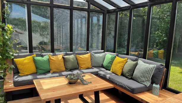 A conservatory with a grey sofa, wooden table, and large windows. - Garden Cottage on Tintern Trails (New Ross)