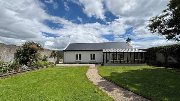A modern house with a sloped roof, a covered patio, and a well-maintained lawn. - Garden Cottage on Tintern Trails (New Ross)