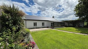 A modern house with a large glass conservatory, a well-maintained lawn, and a stone wall. - Garden Cottage on Tintern Trails (New Ross)