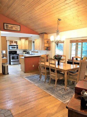 A kitchen with wooden cabinets, a microwave, and an oven. There is a dining table with chairs and a chandelier above.