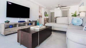 A modern living room with a flat-screen TV, a dark coffee table, a white sofa, and a ceiling fan. - OASIS 2BR/2Bath STEPS from BEACH + Parking @ ESJ (Carolina)