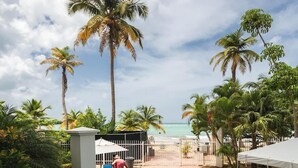 A paved patio area with palm trees, a white tent, and a view of the beach. - OASIS 2BR/2Bath STEPS from BEACH + Parking @ ESJ (Carolina)